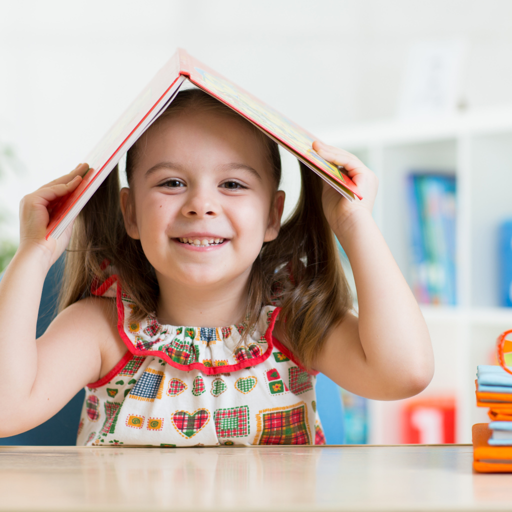 Маленькая улыбающаяся девочка с книгой на голове