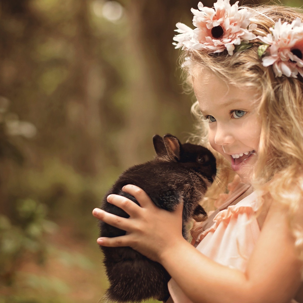 Маленькая улыбающаяся девочка с венком на голове держит кролика