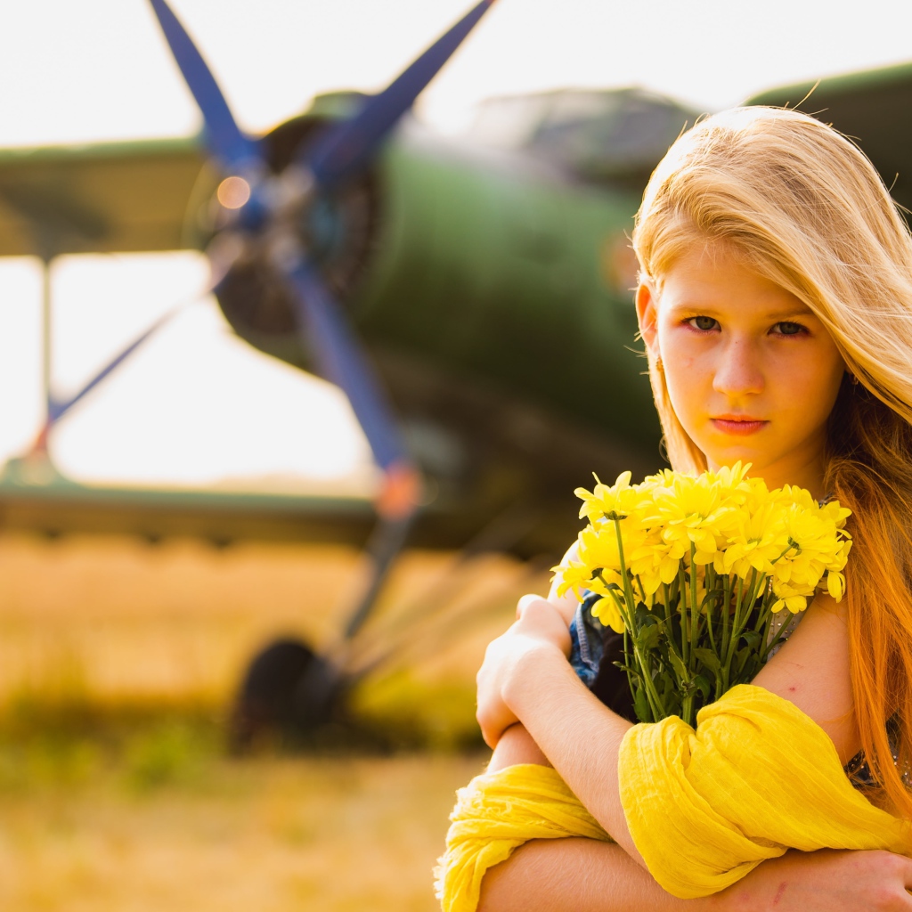Длинноволосая девочка с букетом желтых хризантем на фоне самолета 