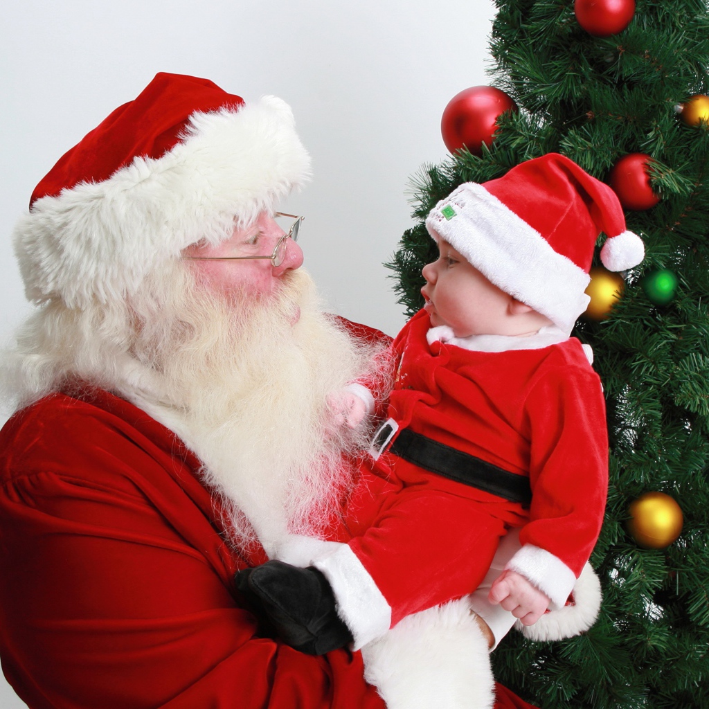 Дед Мороз держит на руках маленького ребенка у елки