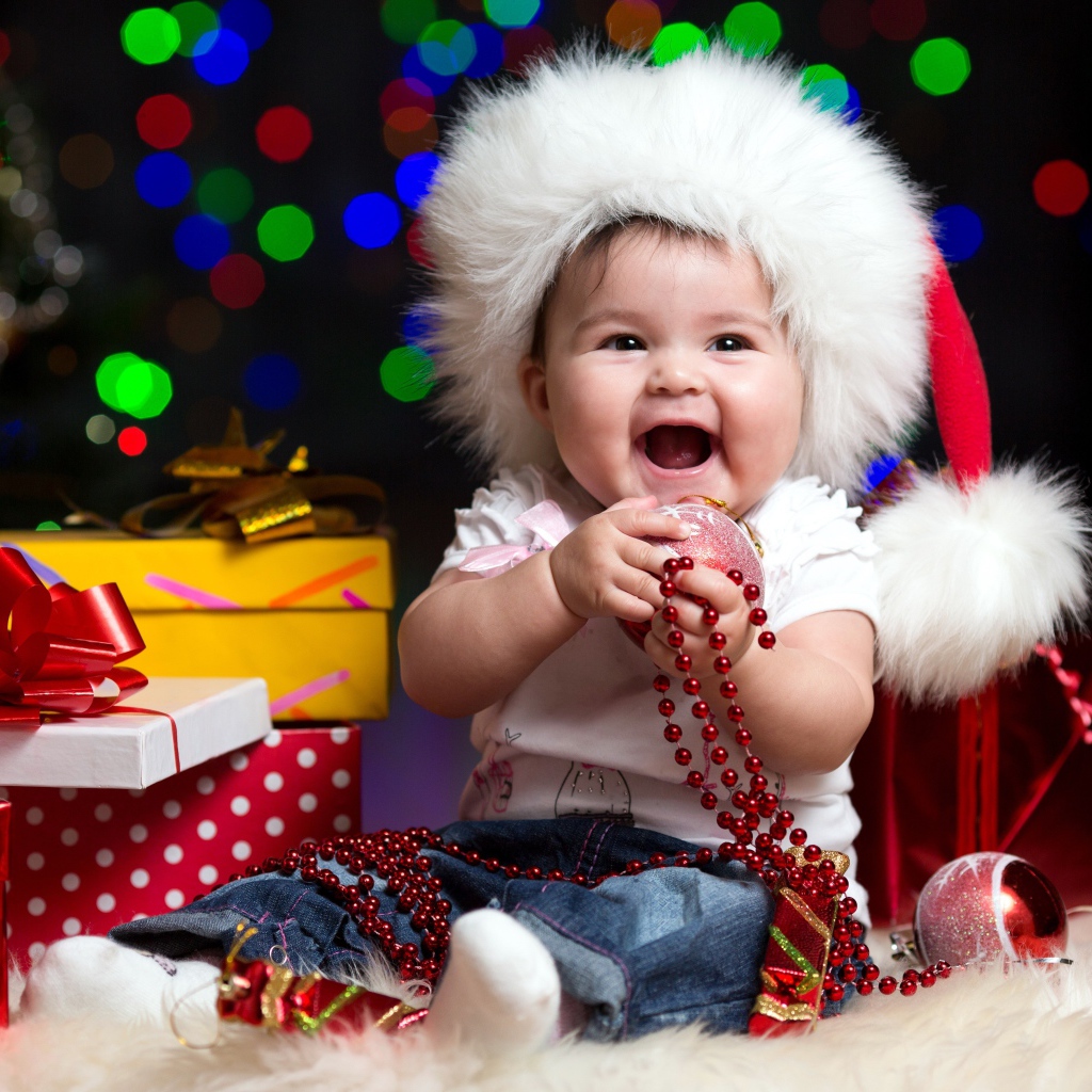 Улыбающийся малыш в новогодней шапке с подарками у елки