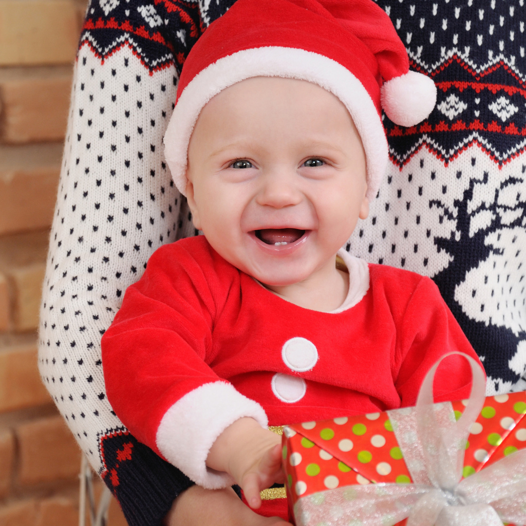 Улыбающийся малыш в костюме с подарком на руках 