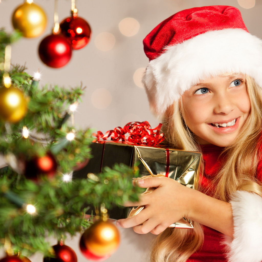 Улыбающаяся девочка блондинка с подарком у елки на новый год 