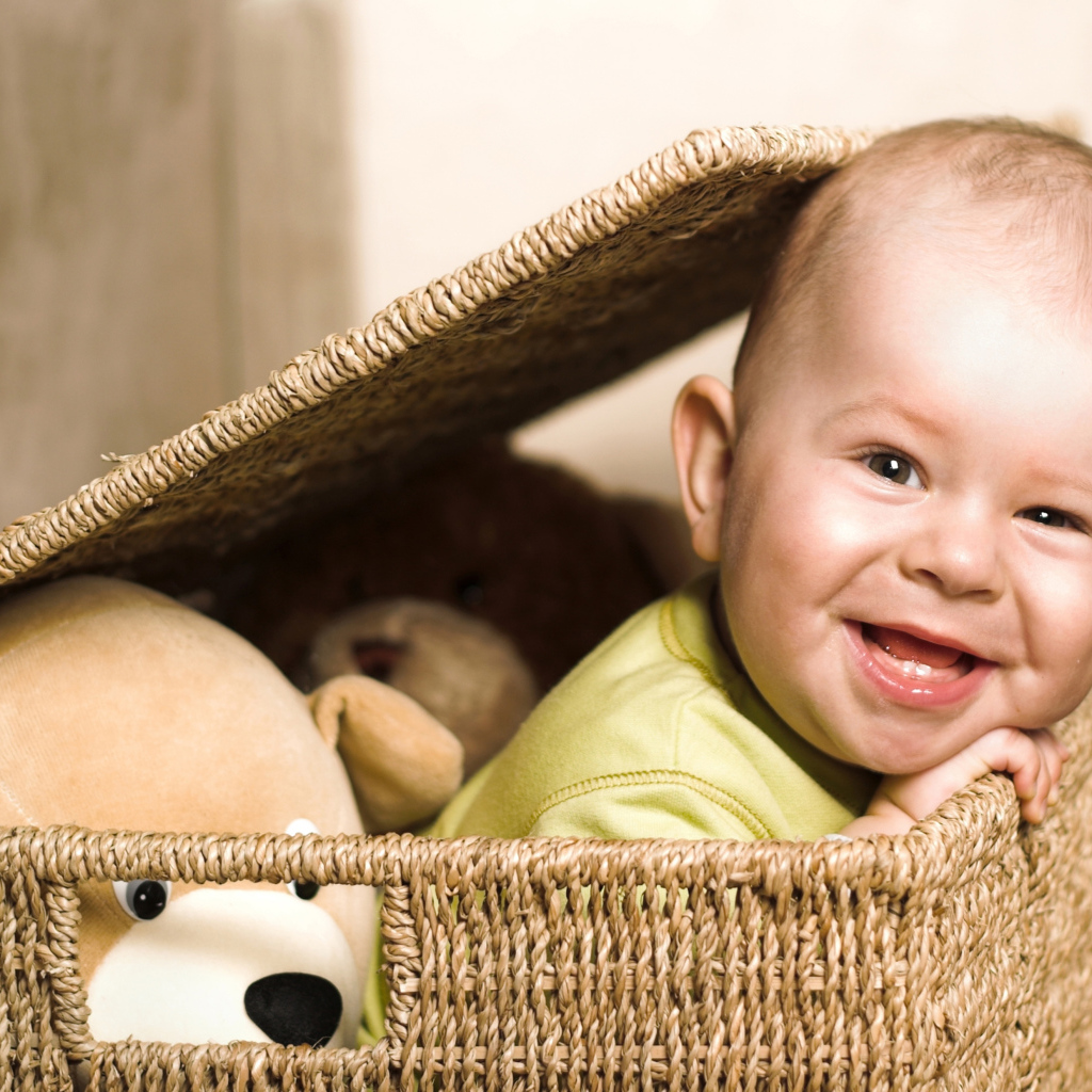 Улыбающийся забавный малыш в плетеной корзине с игрушками