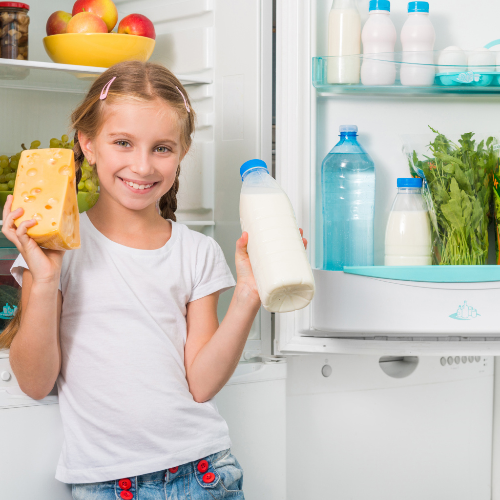 Улыбающаяся девочка у холодильника с сыром и молоком