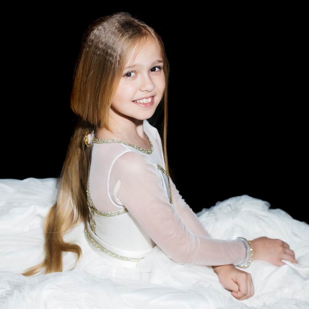 Улыбающаяся девочка в красивом белом платье на черном фоне