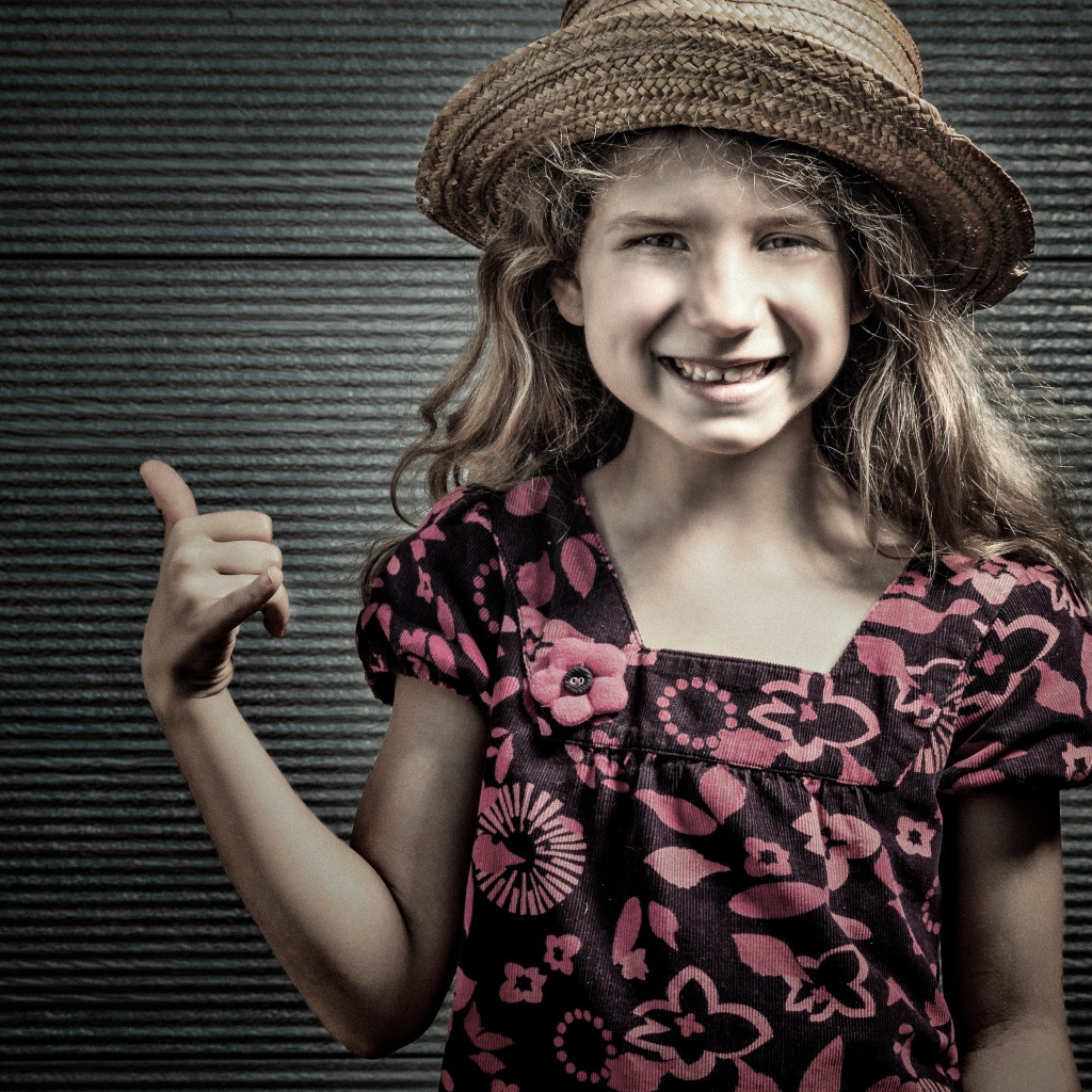 Улыбающаяся девочка в соломенной шляпе у стены 