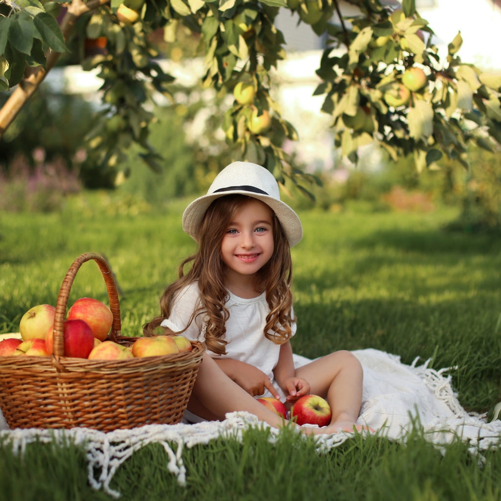 Улыбающаяся девочка сидит на зеленой траве с яблоками