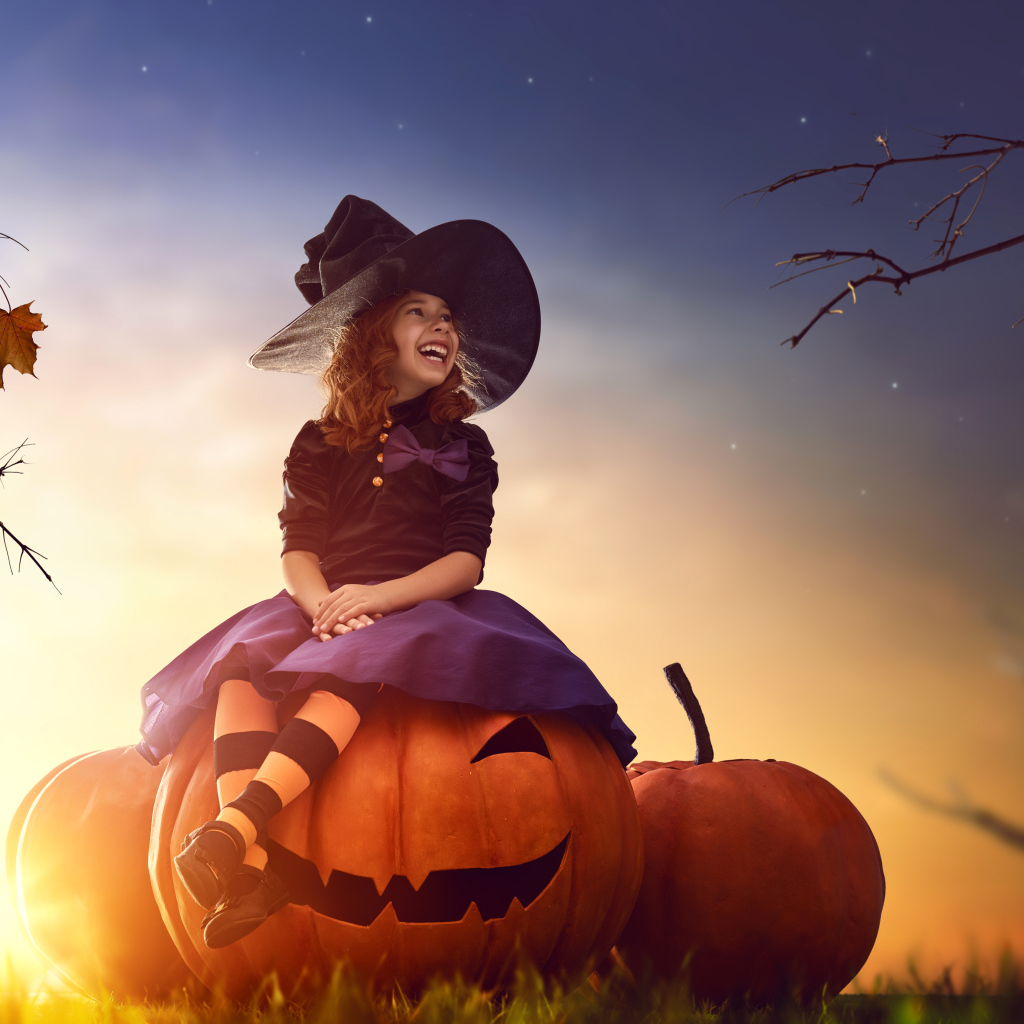 Улыбающаяся девочка сидит на тыкве в костюме на Хэллоуин 