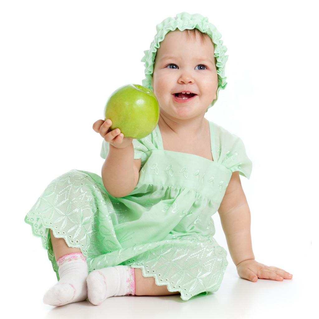Улыбающаяся маленькая девочка в красивом платье с зеленым яблоком в руке