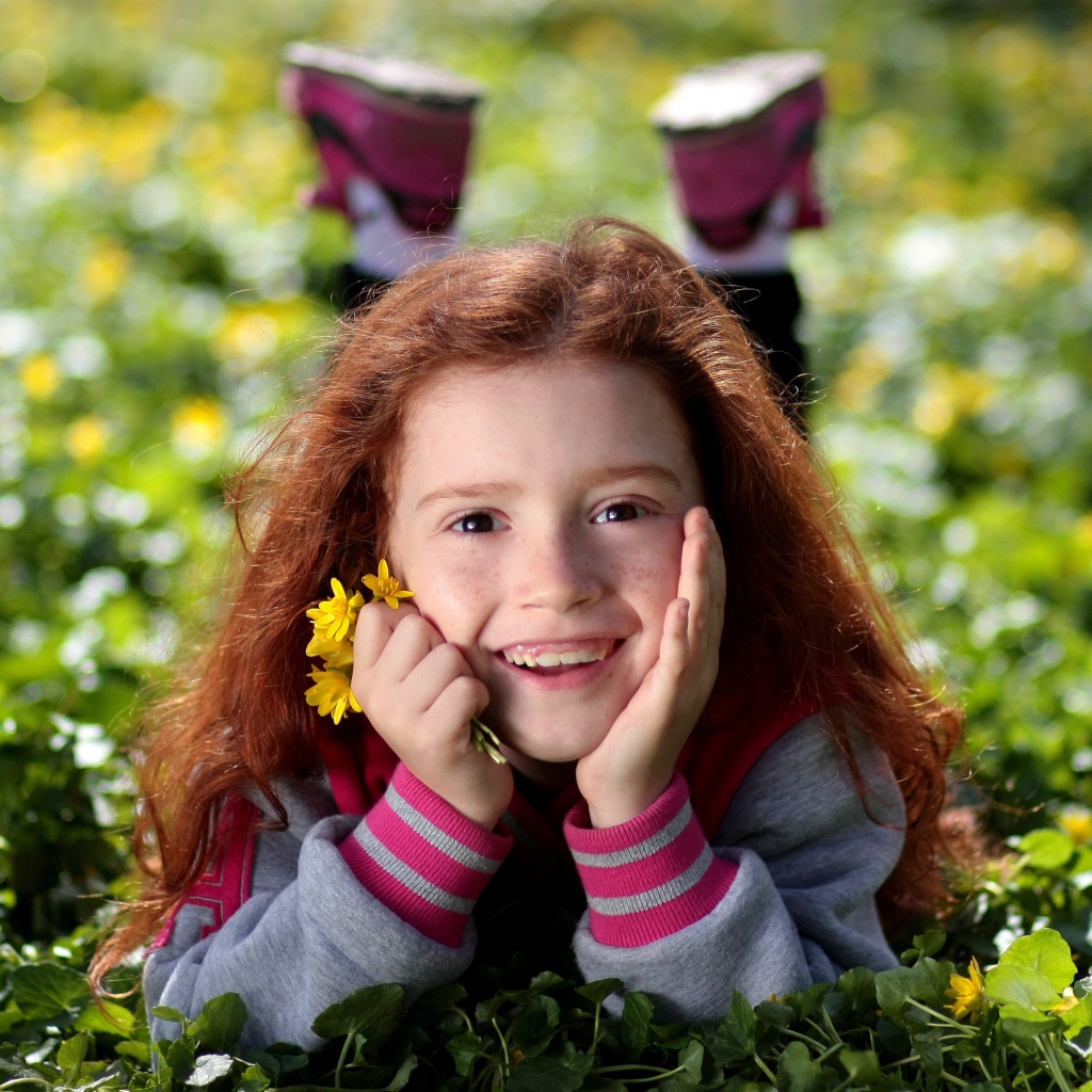 Улыбающаяся рыжеволосая девочка лежит на зеленой траве