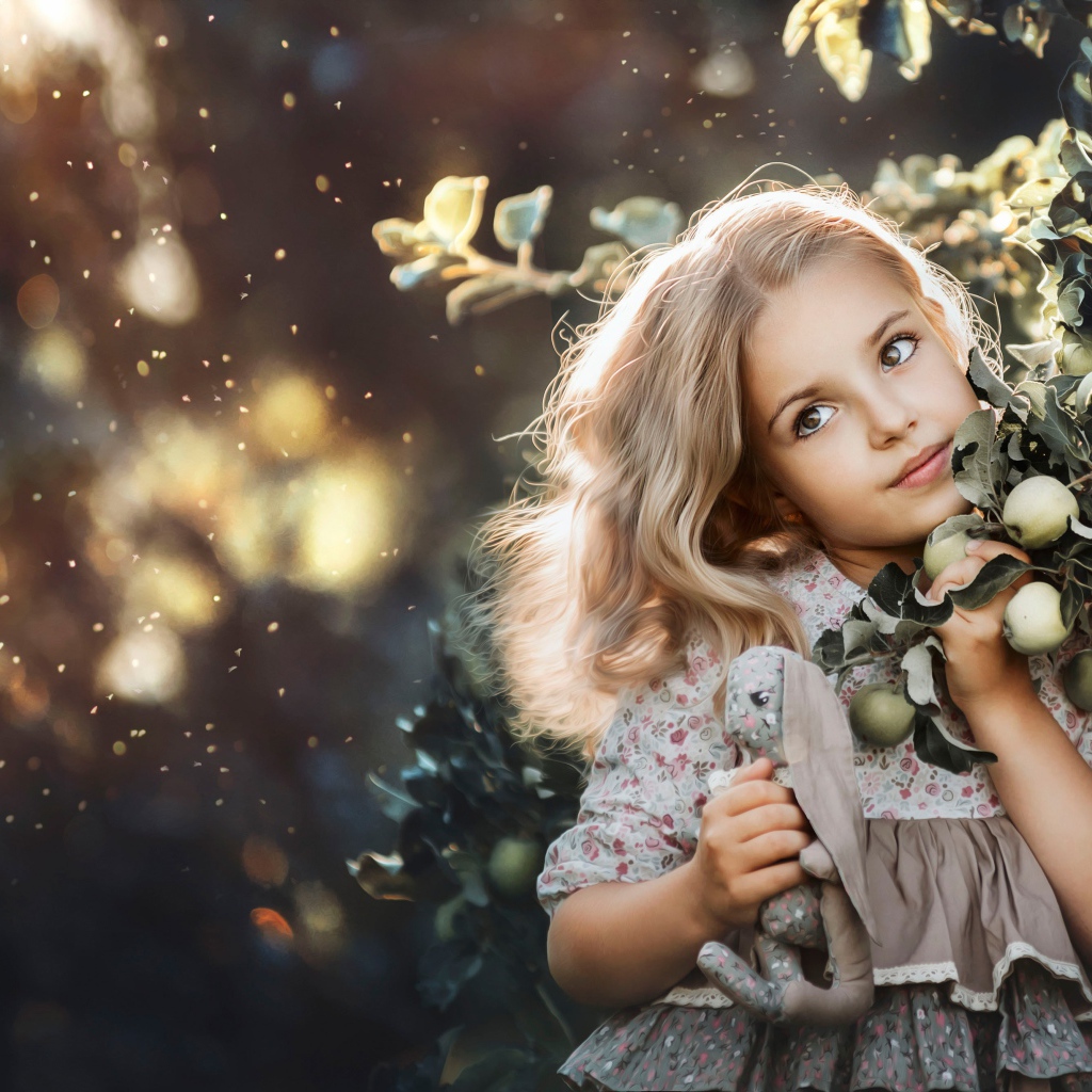 Маленькая девочка стоит у ветки с яблоками