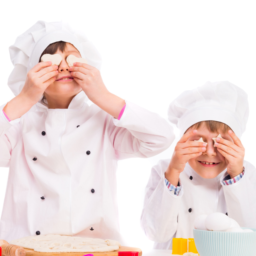 Два маленьких мальчика в костюмах повара на кухне делают печенье