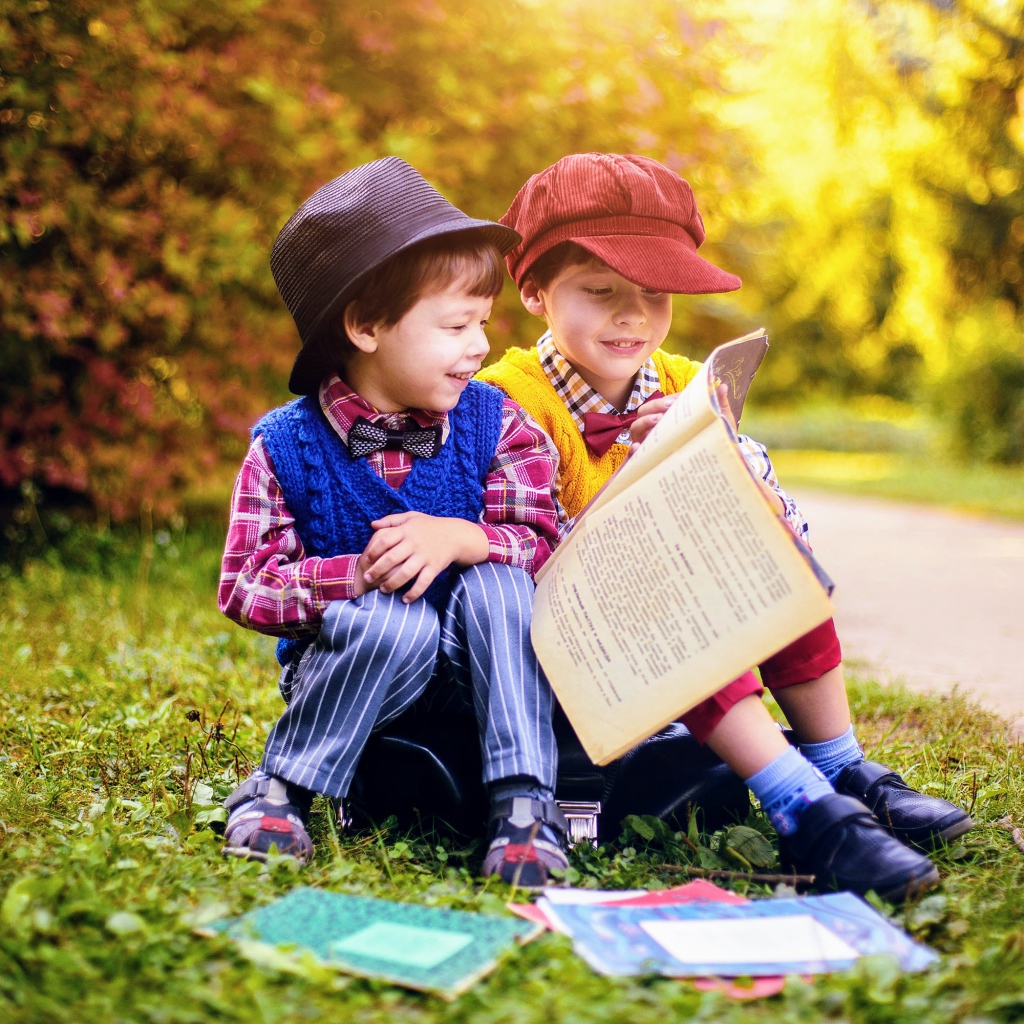 Два маленьких мальчика читают книгу сидя на траве