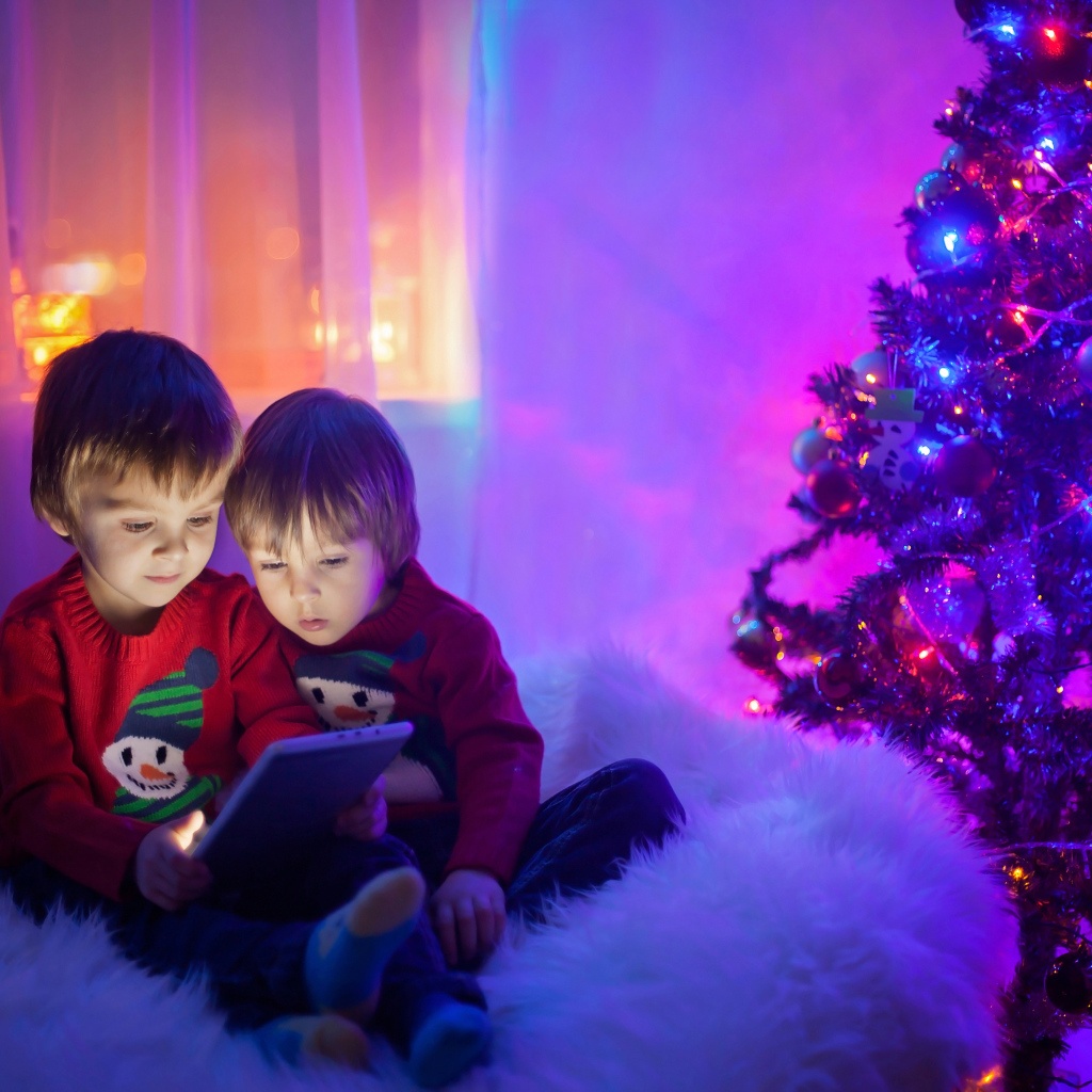 Два маленьких мальчика смотрят мультики у новогодней елки
