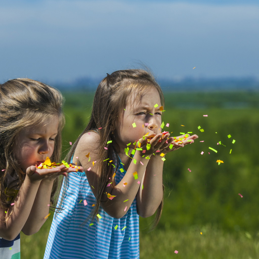 Две маленькие девочки сдувают конфетти  с рук
