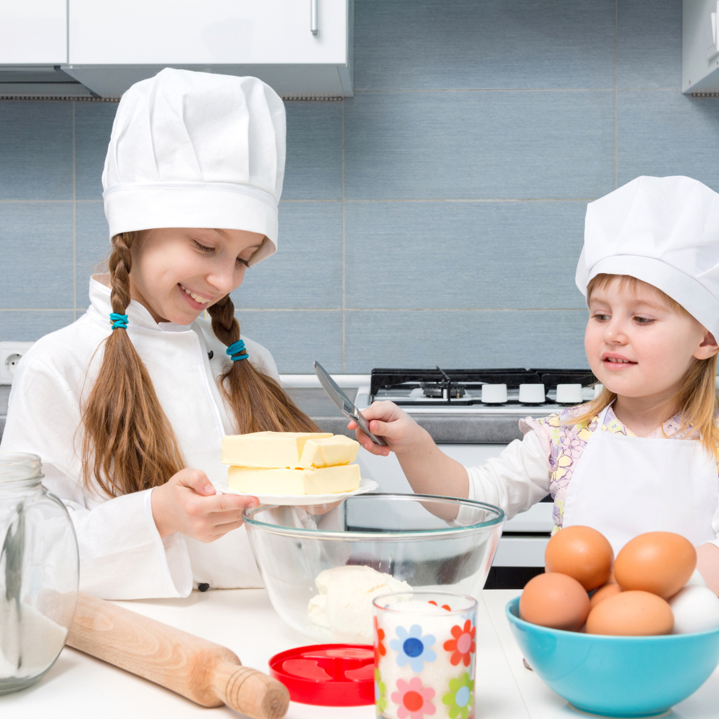 Две маленькие девочки в костюмах повара готовят на кухне