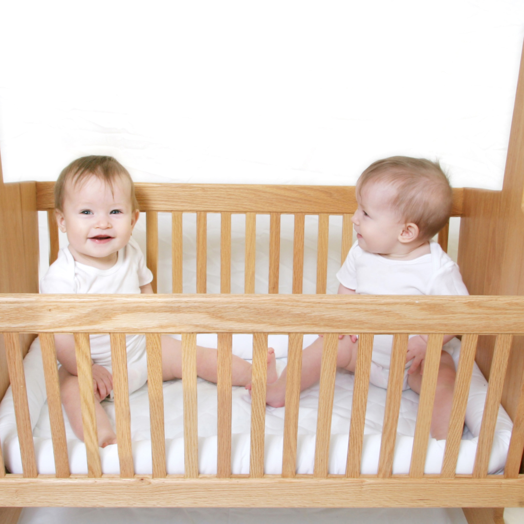 Два улыбающихся малыша в деревянной кроватке