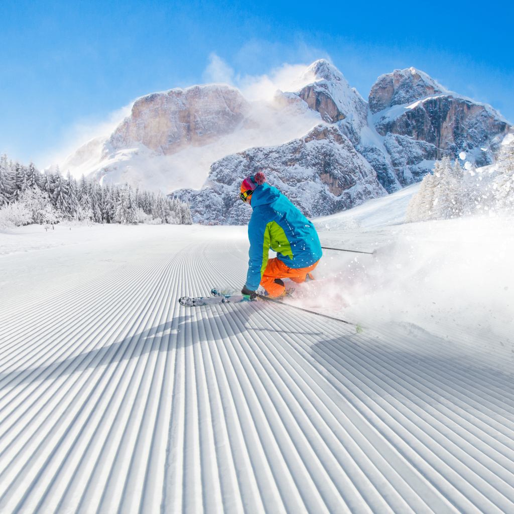 The skier goes down the slope against the backdrop of snow-capped mountains