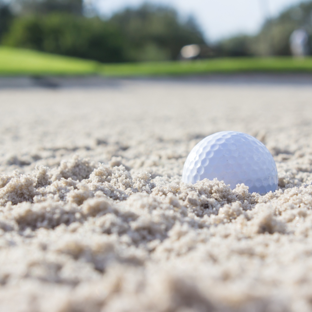 Белый мяч для гольфа лежит на песке