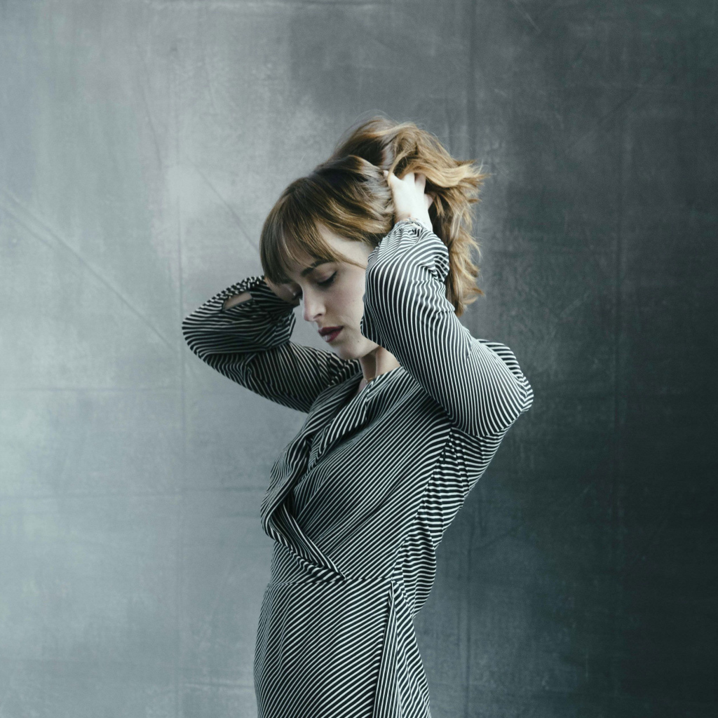 Актриса Дакота Джонсон в платье с руками в волосах