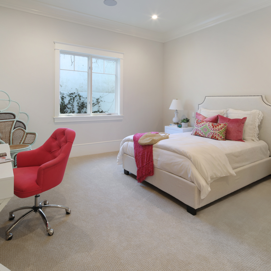 Спальня в светлых тонах с кроватью и столом с красным креслом