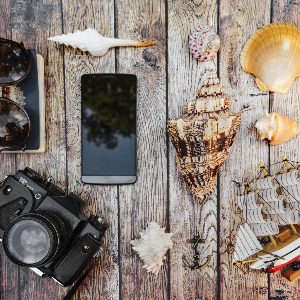 Фотоаппарат, смартфон, ракушки, очки и паспорт на столе