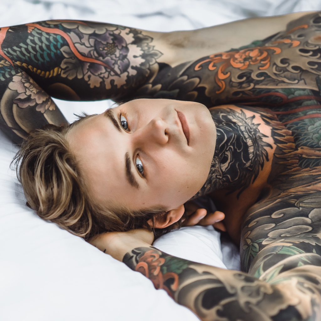 Красивый молодой человек с татуировками на теле лежит на кровати