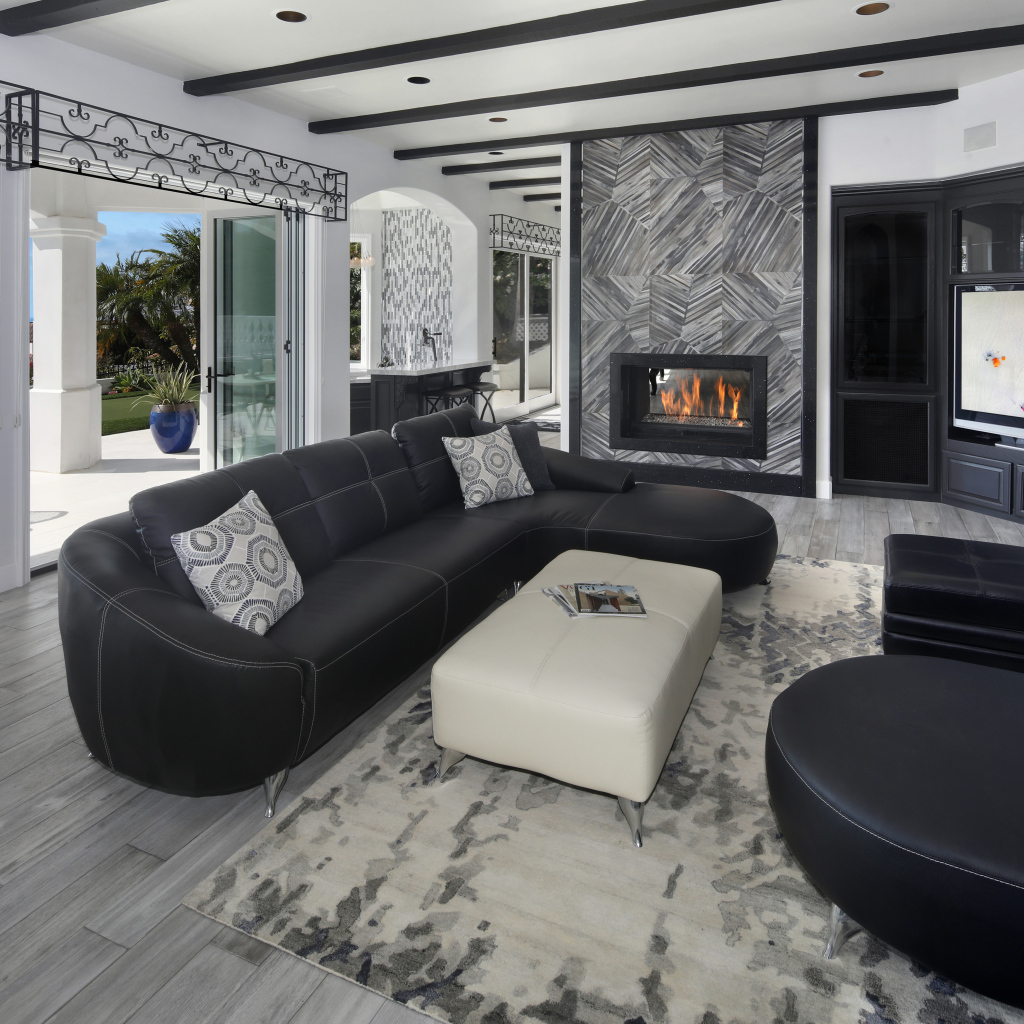 Большая просторная гостиная с черными кожаными диванами, телевизором и камином 