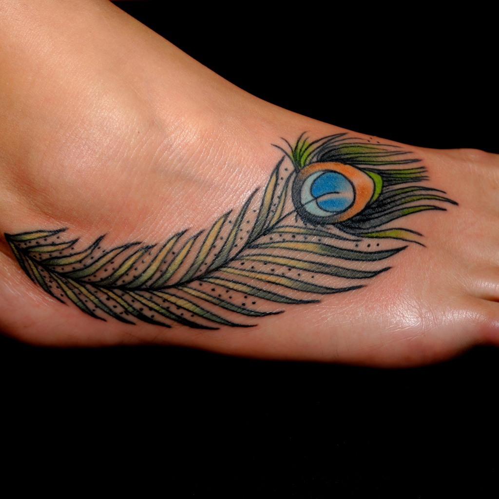 Татуировка перо павлина на ноге на черном фоне