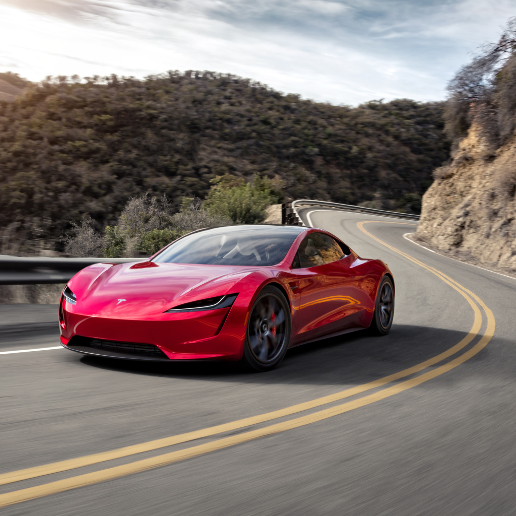 Красный автомобиль Tesla Roadster на трассе у гор 