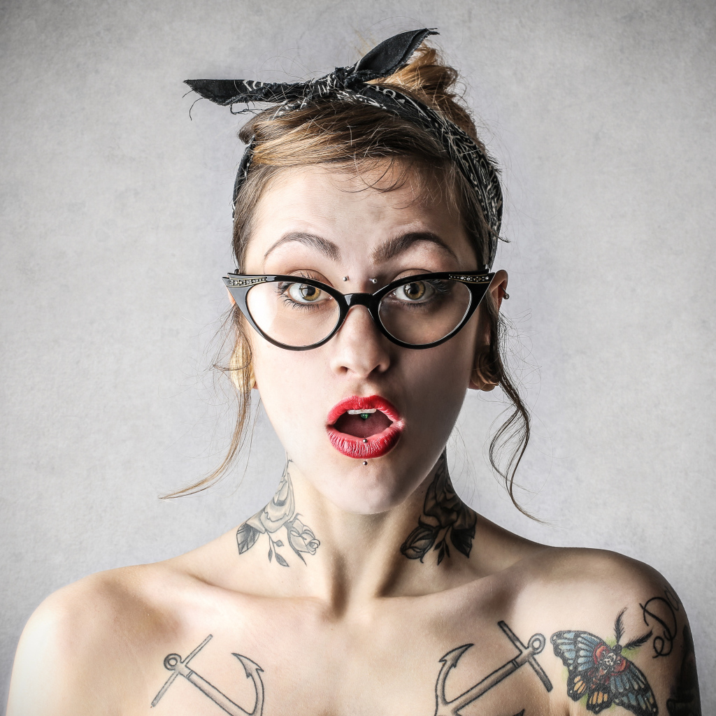 Удивленная девушка в очках с татуировками на теле