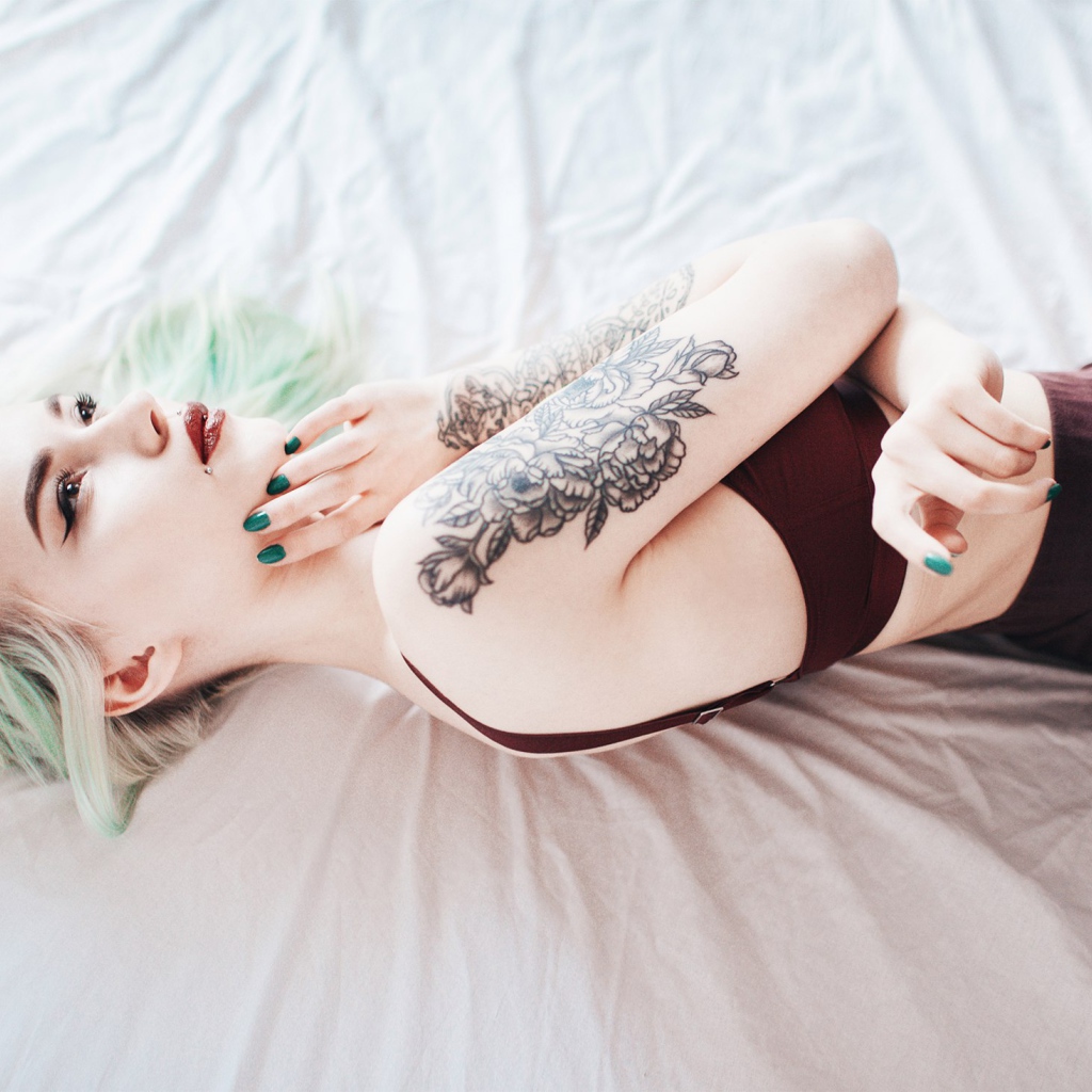 Девушка с татуировкой на руке лежит на кровати 