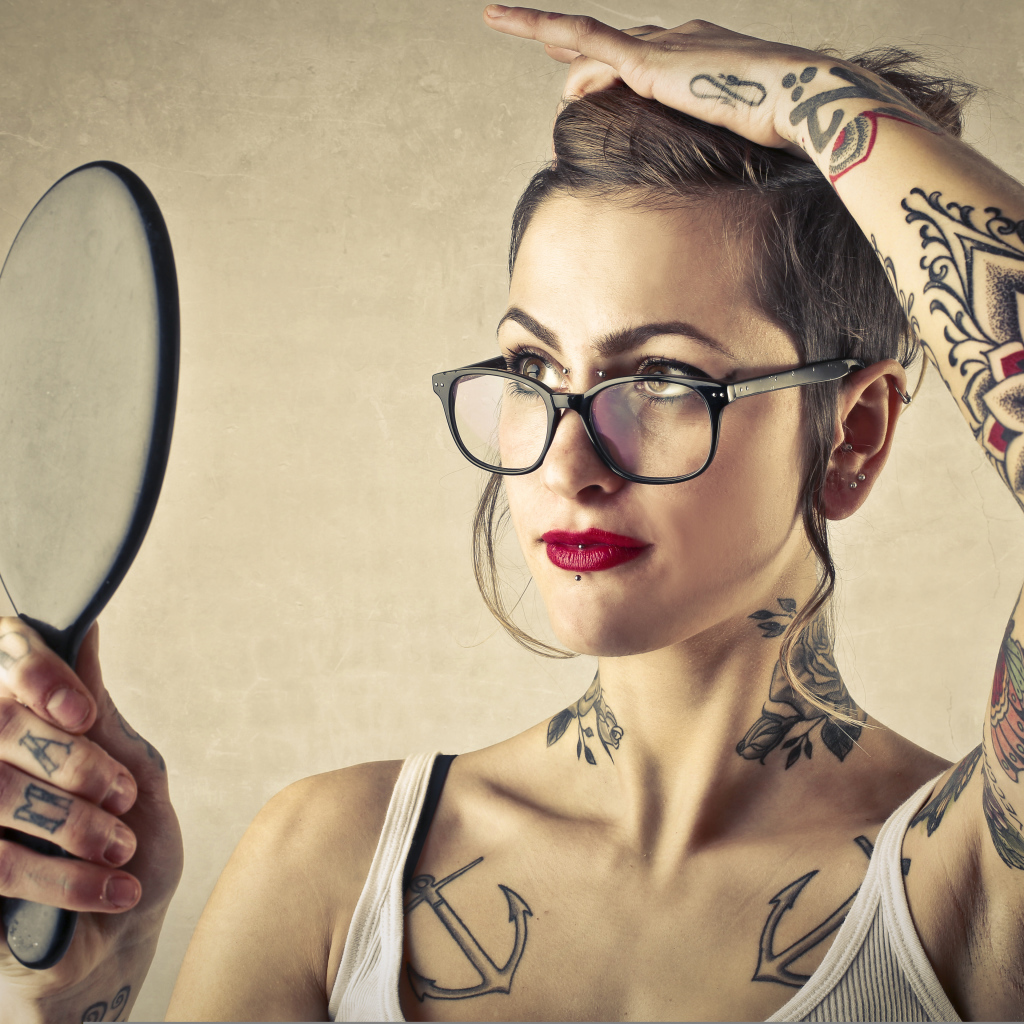 Девушка с татуировками на теле смотрит в зеркало