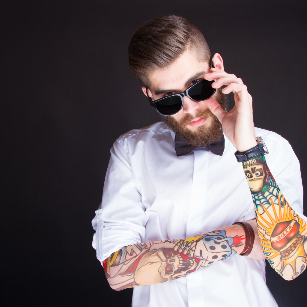 Мужчина в очках с татуировками на руках на сером фоне