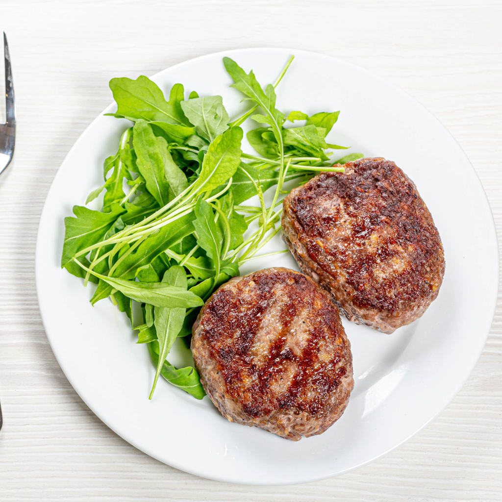 Две котлеты на тарелке с зеленью рукколы 