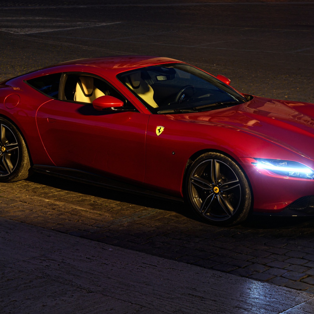Красный автомобиль Ferrari Roma 2020 года с включенными фарами вечером
