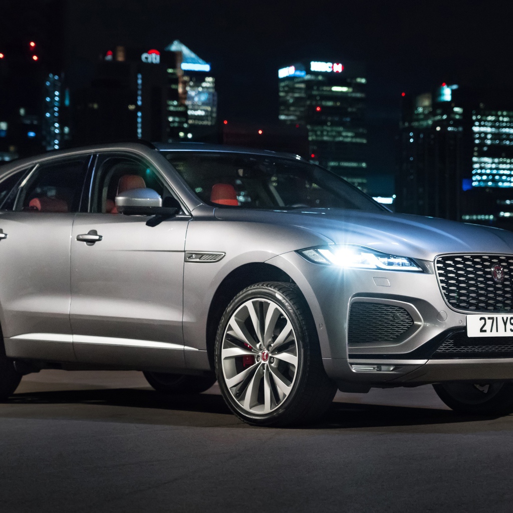 Серебристый Jaguar F-Pace R-Dynamic 2020 года на фоне ночного мегаполиса 