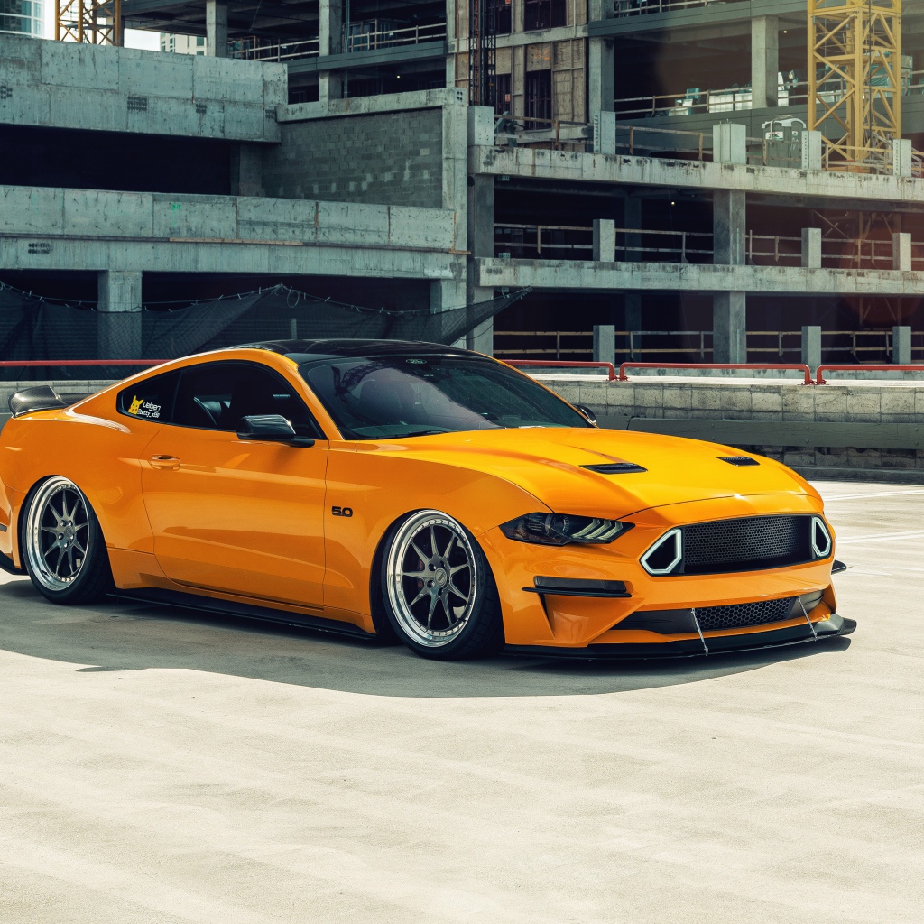 Оранжевый автомобиль Mustang у заброшенного здания 