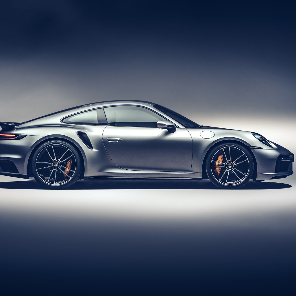 Серебристый автомобиль Porsche 911 Turbo S 2020 года вид сбоку на сером фоне