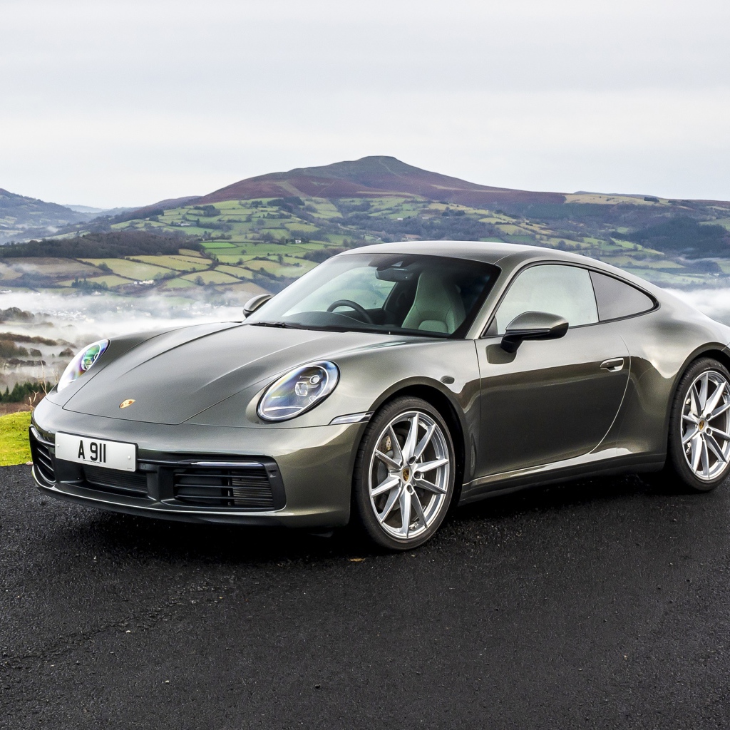 Серебристый автомобиль Porsche 911 Carrera на фоне холмов