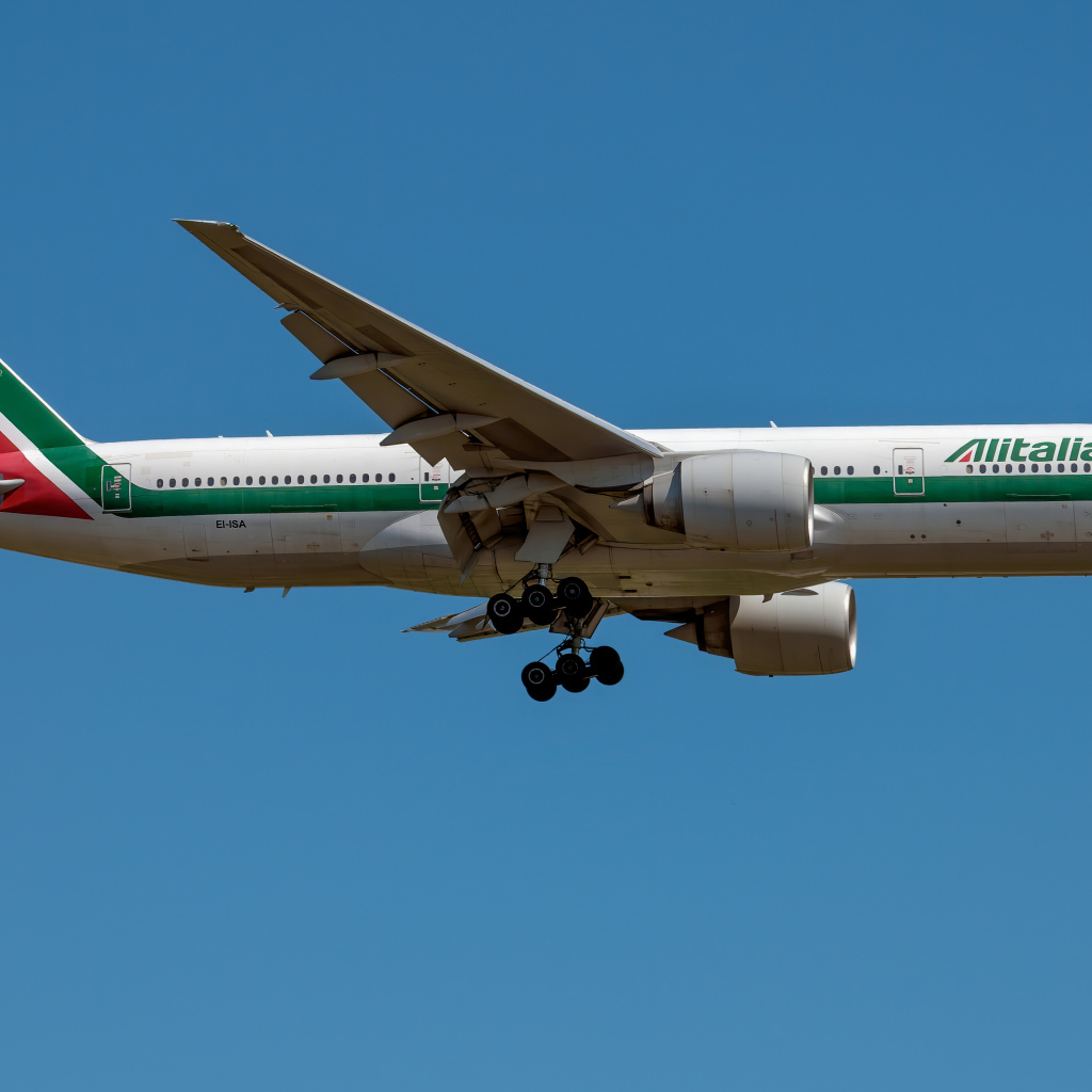 Пассажирский  самолет авиакомпании Alitalia в голубом небе 