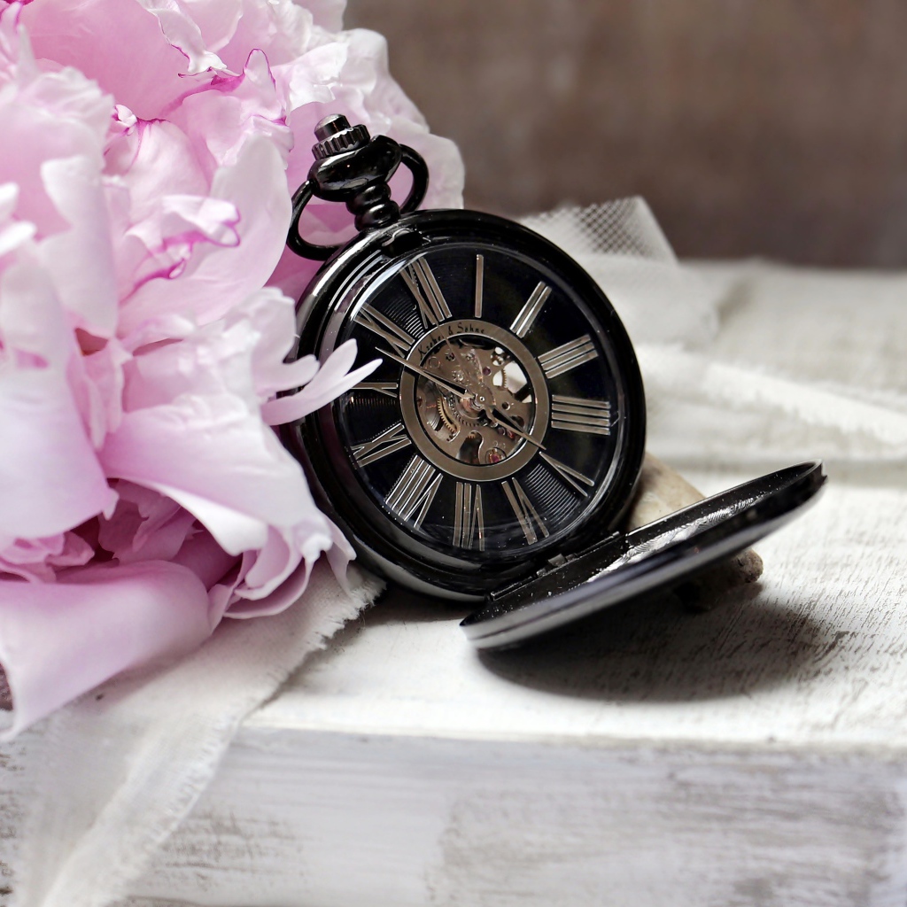 Черные карманные часы с книгой и цветами на столе 