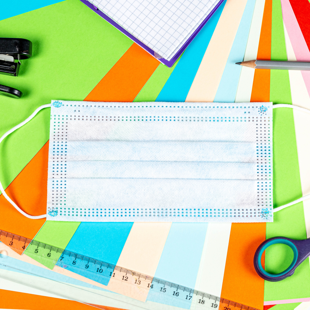 Маска от коронавируса лежит на цветной бумаге с канцелярскими предметами