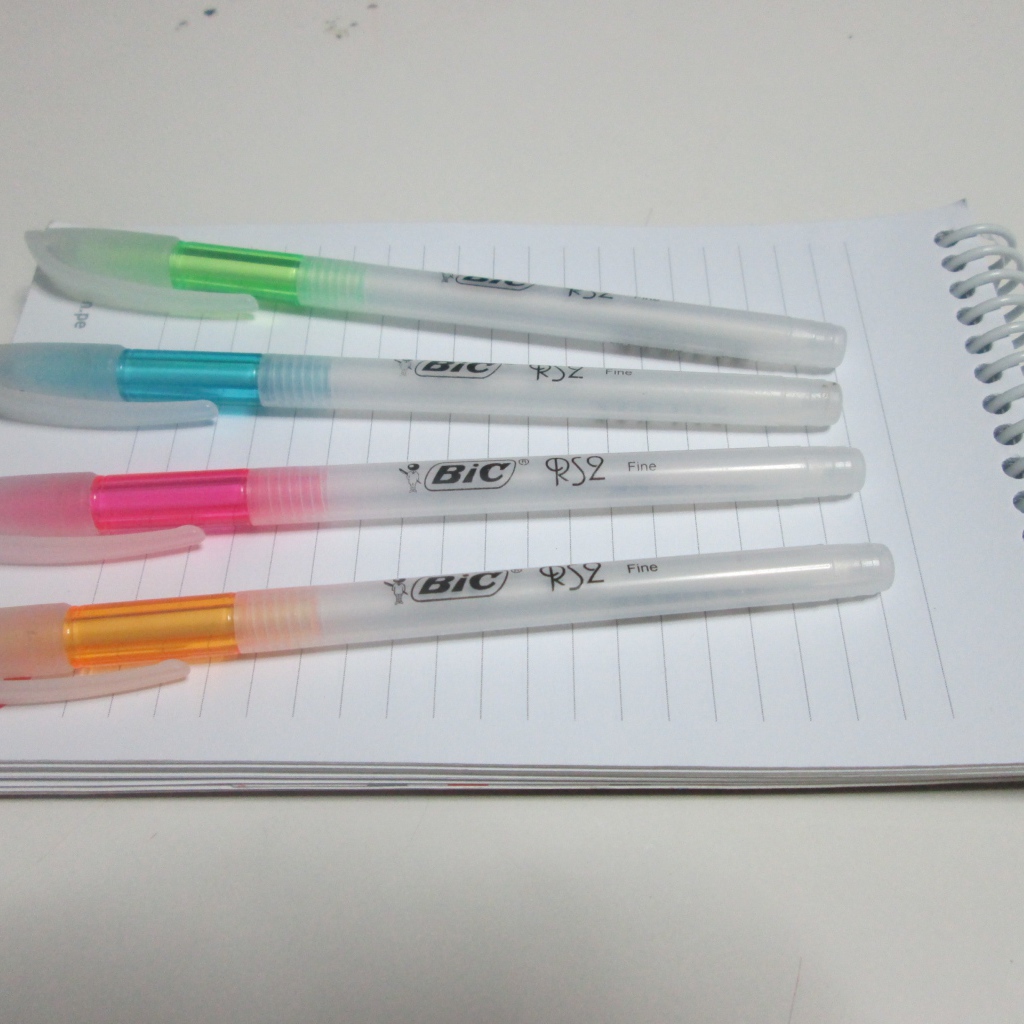 Разноцветные ручки лежат на блокноте на белом фоне 