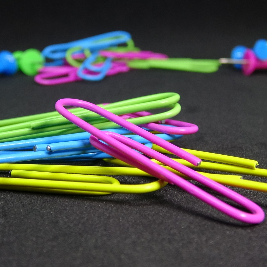 Разноцветные скрепки на черном столе 