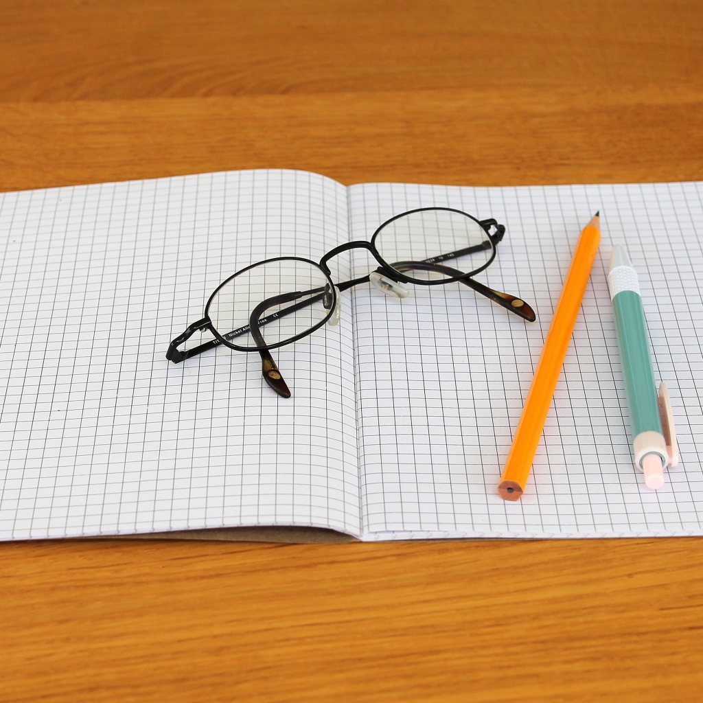 Тетрадь, ручка, карандаш и очки лежат на парте