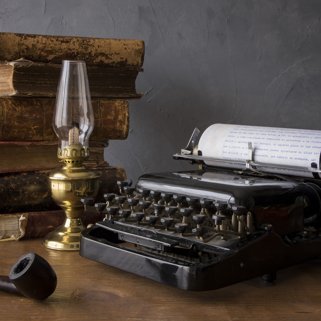 Старая печатная машинка, книги, керосиновая лампа и трубка на столе 