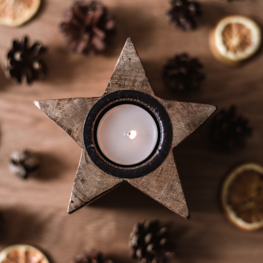 Свеча в форме звезды на столе с шишками и сушеным апельсином