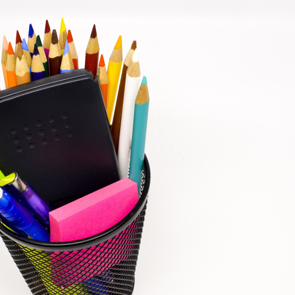 Канцелярские предметы в черном стакане на белом фоне 